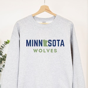 May include: A gray sweatshirt with the text "MINNESOTA WOLVES" in blue and green. The state of Minnesota is depicted in green in the middle of the text.