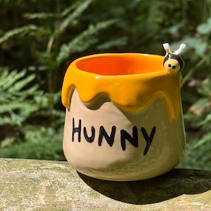 以下が含まれることがあります： クリーム色の斑点のある釉薬が施された、3つのセラミックマグのセット。各マグには、青と緑の葉、黄色の花、赤いベリーなど、異なる手描きのデザインが施されています。マグはシンプルでモダンなデザインです。