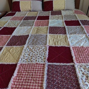 May include: A patchwork quilt with a variety of floral and checkered patterns in shades of red, brown, and cream. The quilt is made with a frayed edge and has a rustic, farmhouse style.