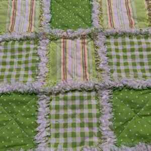 May include: A green and white patchwork quilt with a variety of patterns, including gingham, stripes, and polka dots. The quilt is made with a soft, fluffy fabric and has a white fringe around the edges.