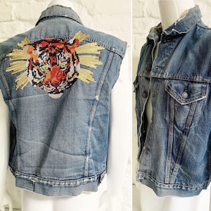 May include: A denim vest with a tiger embroidered on the back. The vest has a distressed look and is sleeveless.