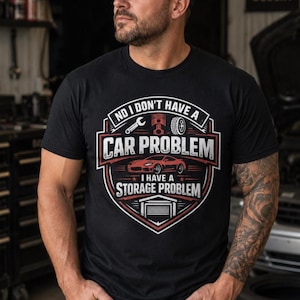 Puede incluir: Una camiseta negra con un diseño gráfico que incluye el texto NO I DON'T HAVE A CAR PROBLEM I HAVE A STORAGE PROBLEM. El diseño presenta una llave inglesa, un pistón, un neumático, un coche deportivo rojo y un icono de garaje en un emblema.
