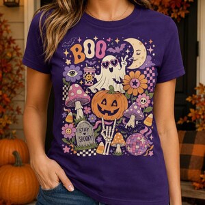 Purple Halloween graphic tee with a smiling pumpkin, spooky ghost, skeleton hand, bats and vintage fall colors.