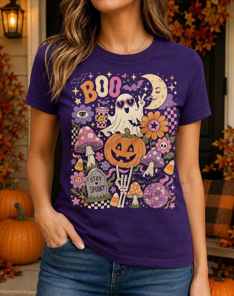Purple Halloween graphic tee with a smiling pumpkin, spooky ghost, skeleton hand, bats and vintage fall colors.