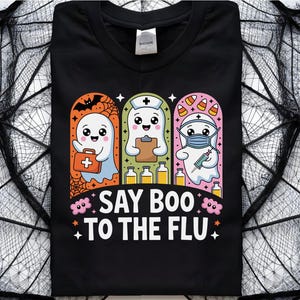 May include: Black t-shirt with a Halloween-themed graphic. The design features three cartoon ghosts, each in a different medical role, with the text "SAY BOO TO THE FLU." The ghosts are set against a backdrop of a spider web.