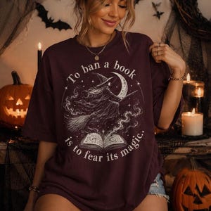 Book lover witch shirt design with vintage Halloween illustration, flying witch, crescent moon, open book and mystical night sky.