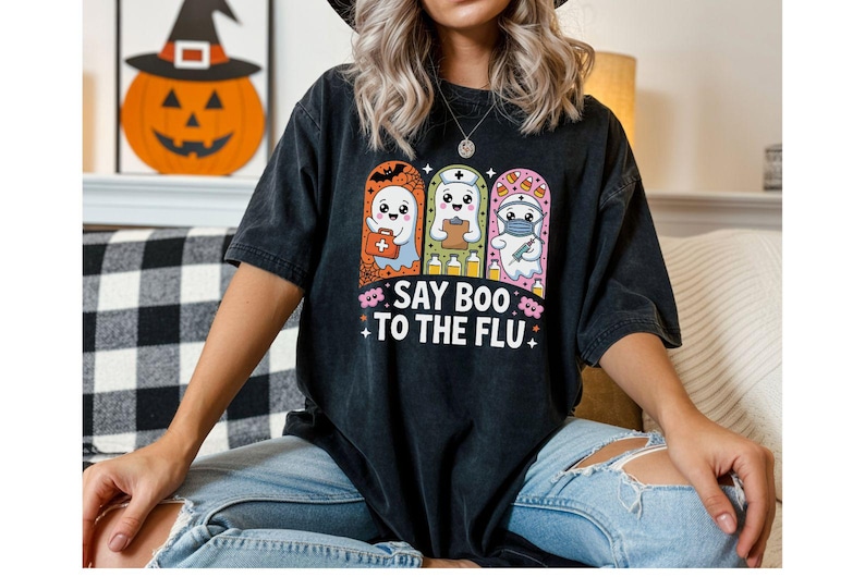 May include: Black t-shirt featuring a Halloween-themed graphic with three cartoon ghosts dressed as a doctor, nurse, and first responder. The text "SAY BOO TO THE FLU" is below the ghosts. A pumpkin with a witch hat is in the background.