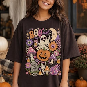 Woman wearing a purple Halloween T-shirt featuring a cute ghost, pumpkin, mushrooms, flowers, moon and colorful retro artwork.
