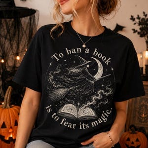 Vintage witch Halloween t-shirt design featuring a flying witch on a broom, crescent moon, stars and open spell book with “To ban a book is to fear its magic” quote.