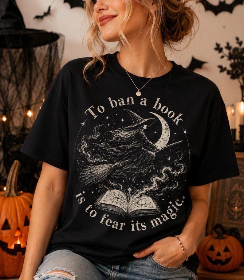 Vintage witch Halloween t-shirt design featuring a flying witch on a broom, crescent moon, stars and open spell book with “To ban a book is to fear its magic” quote.