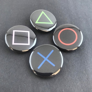 May include: Four glossy black buttons with iconic gaming symbols: a green triangle, a pink square, a red circle, and a blue X. These buttons are arranged in a circular pattern, likely for a gaming console controller.