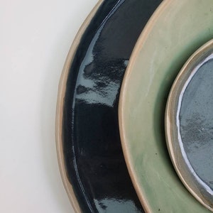 Peut inclure: Trois assiettes en céramique dans différentes nuances de vert et de bleu. Les assiettes sont empilées les unes sur les autres, la plus grande en bas et la plus petite en haut.