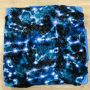 May include: A blue and black fleece blanket with a constellation pattern. The blanket features white and purple stars and constellations on a dark blue background.