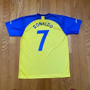 Peut inclure: Un maillot de football jaune et bleu avec le nom "RONALDO" et le num&eacute;ro "7" en bleu. Le maillot a des manches bleues et un col bleu. Le maillot est fait d'une mati&egrave;re l&eacute;g&egrave;re.