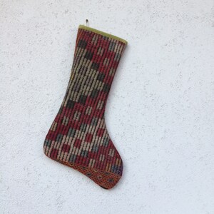 May include: A red, brown, and green patterned stocking with a green cuff. The stocking is made of woven fabric and has a unique, vintage look.