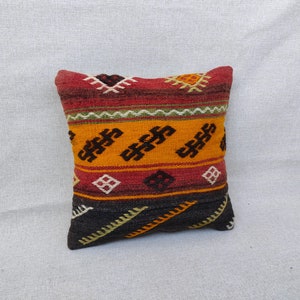 May include: A colourful throw pillow with a geometric pattern in shades of red, orange, yellow, green, and black. The pillow is made of woven fabric and has a traditional design.