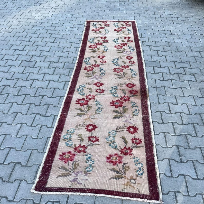 Pu&ograve; includere: Un tappeto rettangolare con motivo floreale, sfondo color crema e bordo bordeaux. Il tappeto presenta motivi floreali ripetuti in rosso, blu e verde. Adatto per un corridoio o un ingresso.
