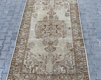 Puede incluir: Una alfombra rectangular con un fondo beige descolorido y complejos patrones geométricos y florales en color marrón. El diseño incluye un medallón central rodeado de motivos simétricos y un borde ancho y detallado en los cuatro lados.