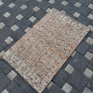 May include: A rectangular area rug featuring a repeating geometric pattern in shades of tan, beige, and faded blue. The design includes intricate floral motifs and decorative borders at both ends, showcasing a weathered, low-pile textile texture.