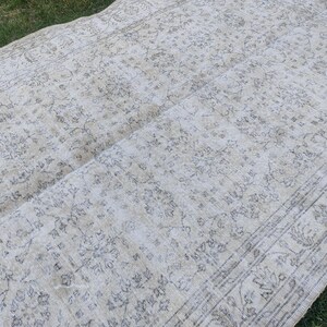 May include: A rectangular, vintage-style rug with a faded, floral pattern in shades of cream and gray. The rug has a distressed look, with visible wear and tear, and is laid out on a grassy surface.