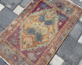 May include: A rectangular area rug featuring a central medallion in shades of ochre, slate blue, and sage green, set against a deep burgundy background. The rug has a decorative border with intricate geometric patterns and short white fringe.