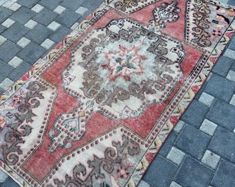 Puede incluir: Una alfombra rectangular con un diseño de medallón central en tonos rojo coral, crema y marrón apagado. La alfombra muestra intrincados patrones geométricos y florales con una textura desgastada y un borde decorativo.