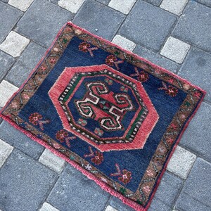 May include: A rectangular area rug featuring a deep blue field with a central pink octagonal medallion containing intricate geometric patterns in green, white, and red. The border displays a brown floral motif, and the edges have pink fringe.