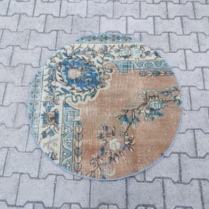 Può includere: Tappeto rotondo dall'aspetto vintage e usurato. Il tappeto presenta un campo centrale color pesca con motivi floreali e a vite blu e crema. Il bordo è azzurro con altri disegni floreali. Il tappeto ha un aspetto morbido e usurato.