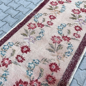 Pu&ograve; includere: Un tappeto vintage con un motivo floreale. Il tappeto presenta uno sfondo rosa chiaro con un motivo ripetuto di fiori rossi e blu. Il bordo &egrave; di colore bordeaux scuro, aggiungendo una cornice a contrasto al design floreale.