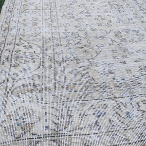 May include: A vintage beige rug with an intricate floral pattern. The rug features a distressed look with faded colors and a detailed border. The design includes shades of beige, brown, and blue, creating a classic, aged aesthetic.