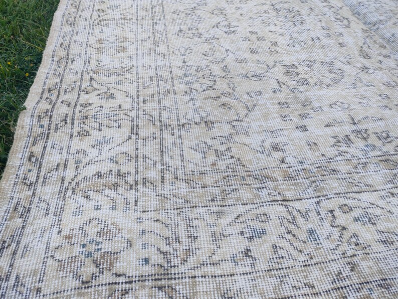 May include: A vintage beige rug with an intricate floral pattern. The rug features a distressed look with faded colors and a detailed border. The design includes shades of beige, brown, and blue, creating a classic, aged aesthetic.
