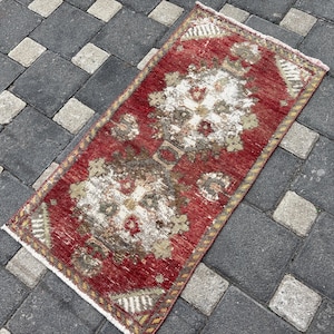 Op de afbeelding: Een rechthoekig vloerkleed met een dieprode achtergrond en ingewikkelde, symmetrische patronen in witte, beige en gedempte bruintinten. Het kleed heeft een geweven textuur met korte franjes aan beide uiteinden en een decoratieve rand.