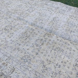 May include: A large, rectangular, vintage rug with a faded floral pattern in shades of cream, beige, and gray. The rug has a distressed appearance, with visible wear and tear, and a detailed border.