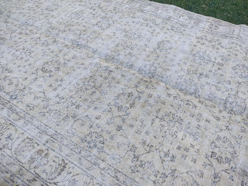 May include: A large, rectangular, vintage rug with a faded floral pattern in shades of cream, beige, and gray. The rug has a distressed appearance, with visible wear and tear, and a detailed border.