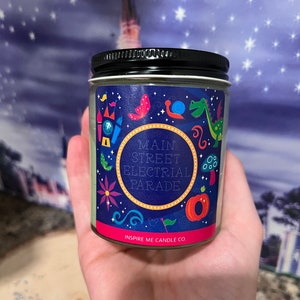May include: A green candle with a black lid and a colorful label that says "Main Street Electrical Parade" and "Inspire Me Candle Co."