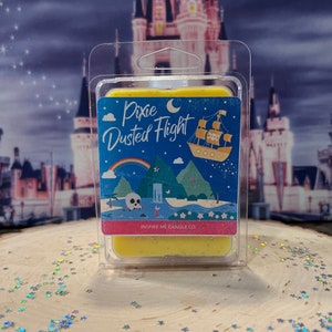 Może przedstawiać: Żółty wosk w przezroczystym plastikowym opakowaniu z kolorową ilustracją statku, czaszki i wodospadu. Tekst na wosku brzmi "Pixie Dusted Flight" i "Inspire Me Candle Co."