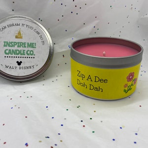 May include: A yellow candle tin with the text "Zip A Dee Doh Dah" and a pink floral design. The candle is pink and has a single wick.