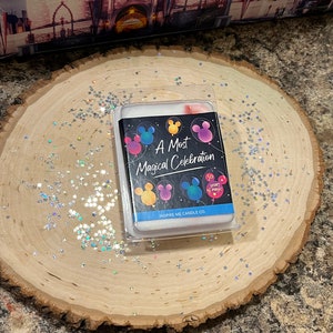 May include: A white candle with a black label that says "A Most Magical Celebration" with Mickey Mouse ears and balloons. The label also says "Inspire Me Candle Co."