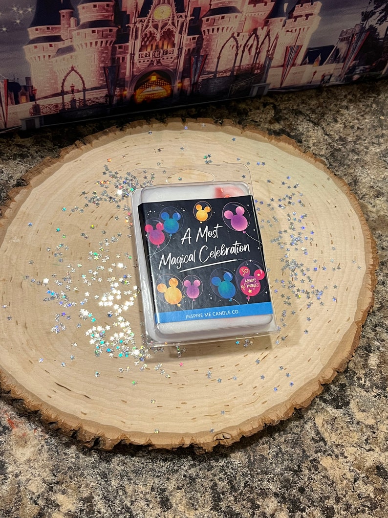 May include: A white candle with a black label that says "A Most Magical Celebration" with Mickey Mouse ears and balloons. The label also says "Inspire Me Candle Co."