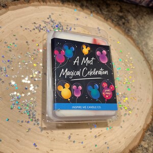 May include: A white wax melt with a black background featuring Mickey Mouse balloons and the text "A Most Magical Celebration" and "50 Years of Magic". The wax melt is packaged in a clear plastic container with the text "Inspire Me Candle Co."