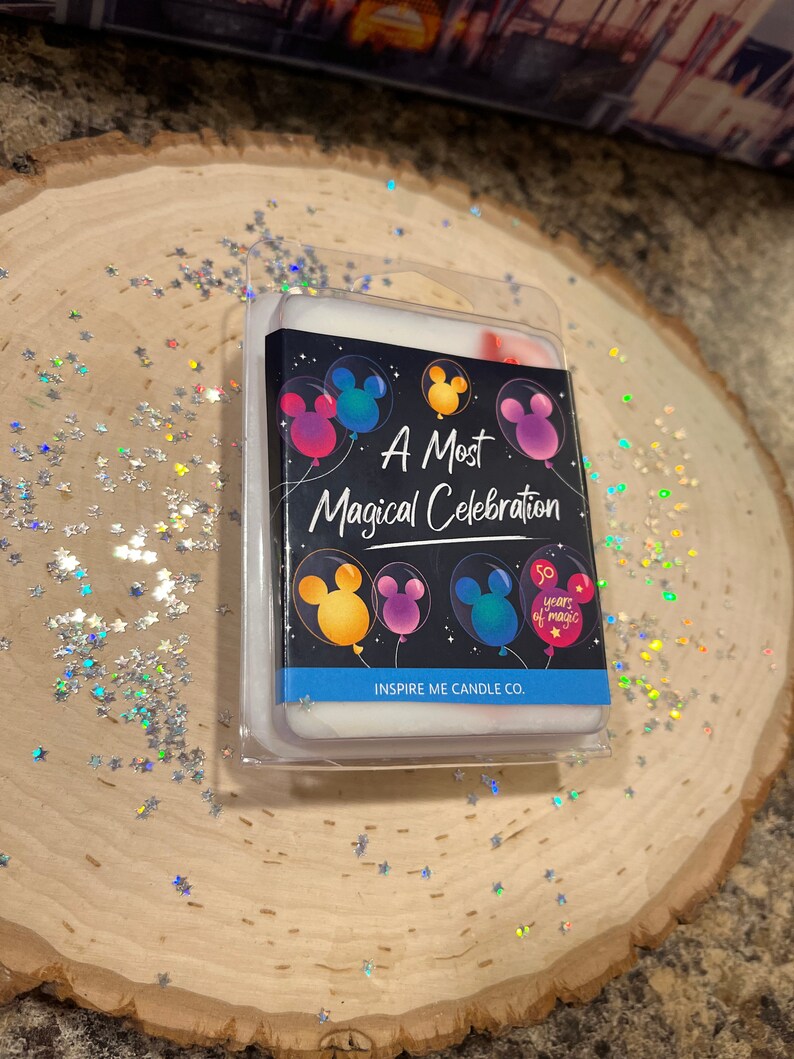 May include: A white wax melt with a black background featuring Mickey Mouse balloons and the text "A Most Magical Celebration" and "50 Years of Magic". The wax melt is packaged in a clear plastic container with the text "Inspire Me Candle Co."