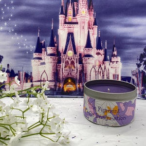 May include: Purple candle in a tin container with a white background and a purple dragon design. The text on the container reads "The Figment of Imagination".