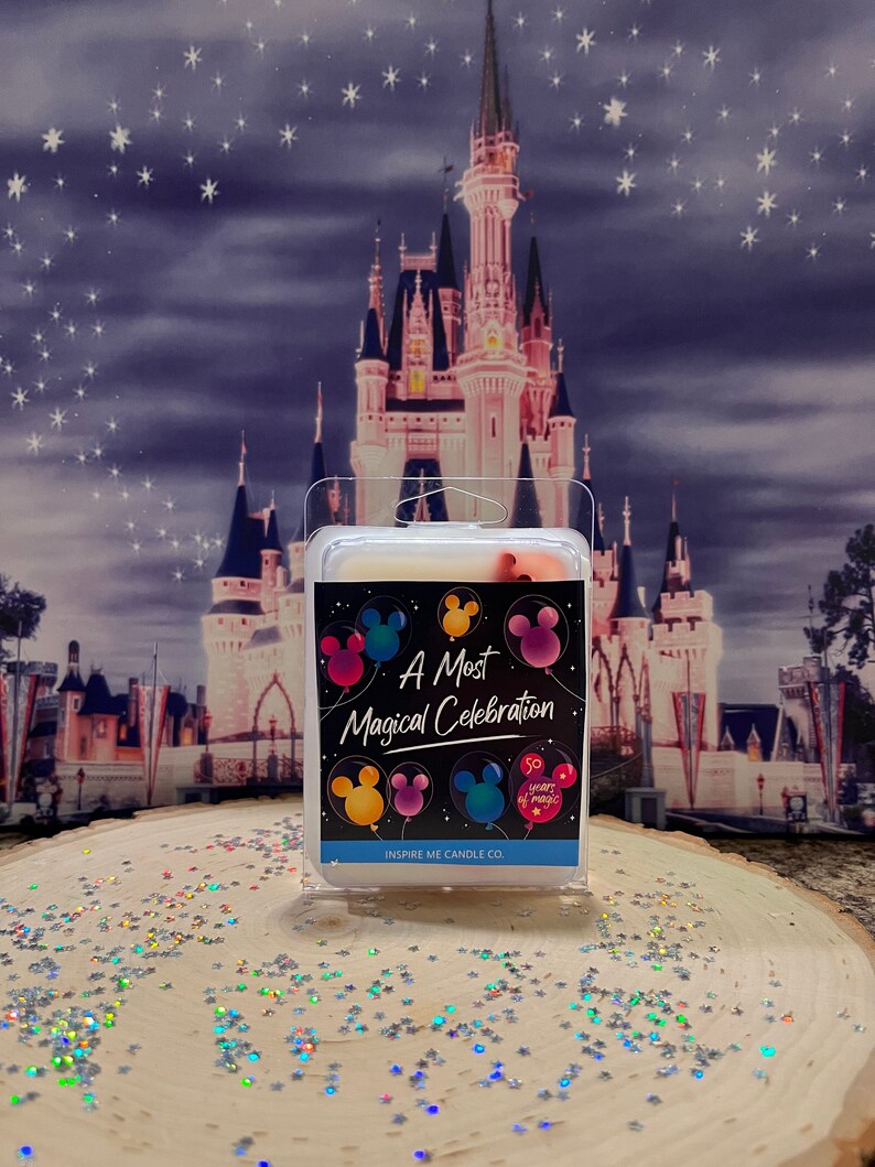 May include: A white candle with a black label that says "A Most Magical Celebration" with Mickey Mouse balloons and the text "50 Years of Magic". The candle is in front of a picture of Cinderella's Castle.
