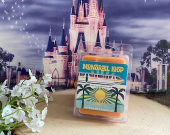 May include: An orange wax melt in a clear plastic clamshell. The label says "Monorail Loop" with a monorail, palm trees, and a sun graphic. The background shows a castle and a starry sky. The product is on a wooden slice.