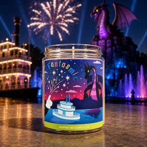 May include: A clear glass candle jar with a label featuring the text Fantasmic and Inspire Me Candle Co. The label displays a cartoon illustration of a white steamboat, a gloved hand, a purple dragon, and fireworks against a night sky.