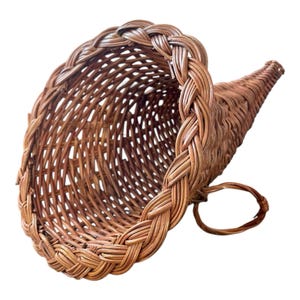 May include: A brown woven cornucopia basket, ideal for decorative displays. The basket is made of woven wicker and features a braided rim and handle. The basket is empty and has a curved shape, with a wide opening and a tapered end.