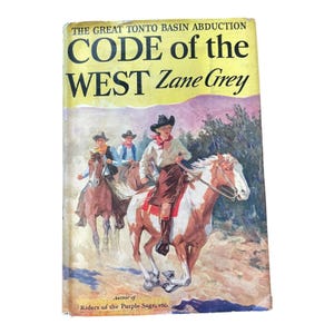 May include: A vintage hardcover book titled Code of the West by Zane Grey, featuring The Great Tonto Basin Abduction. The cover art depicts three figures on horseback in a desert landscape with a yellow sky and the text Author of Riders of the Purple Sage.