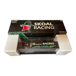 Op de afbeelding: Een zwarte doos met de woorden "SKOAL RACING" in wit en groen. De doos bevat een 1:96 schaal raceauto-transporter in een display case. De display case wordt ondersteund door wit schuim.