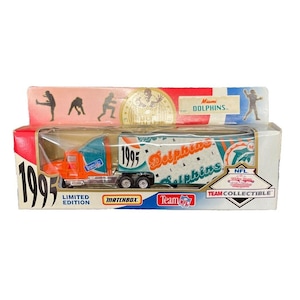 以下が含まれることがあります： オリジナルパッケージに入った、Matchbox Team NFL Miami Dolphinsのセミトレーラーの玩具。トラックはオレンジとティールで、トレーラーには「1995 Dolphins」のグラフィックが描かれています。パッケージには「Limited Edition」と「Team NFL Collectible」と書かれています。