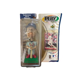 Puede incluir: Una figura de bobblehead de los Cardenales de San Luis en una funda de plástico transparente, sosteniendo un bate de béisbol. La figura lleva una gorra y un uniforme azules. Se incluye una tarjeta coleccionable. El embalaje también incluye una tarjeta de béisbol.